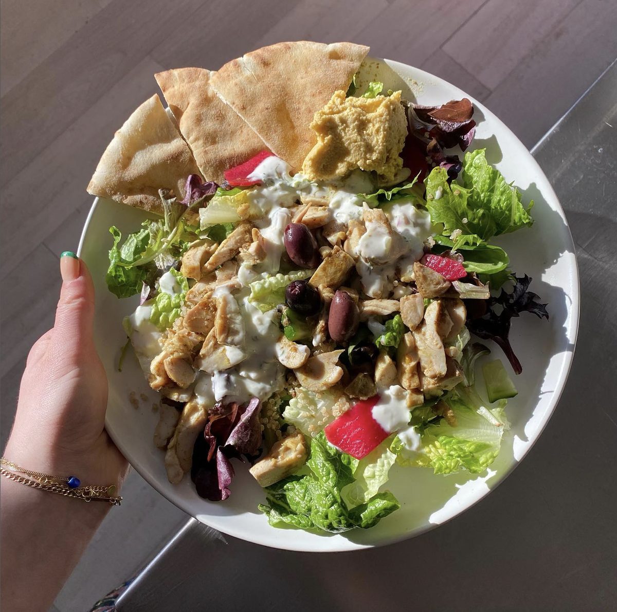 A generous plate of organic greens with pita and hummus, held up at the cafe